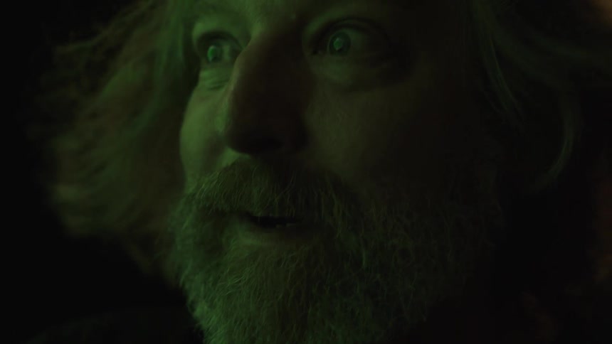A bearded middleaged man with long hair stands outdoors at night excited as the wind blows his hair around