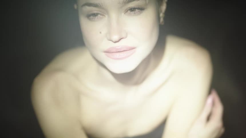 A shot of a woman with her hair pulled back and her lips slightly parted is shown she is looking directly at the camera the video then cuts to a closeup of her face as she appears to be in a state of distress with her eyes wide open and her hand raise