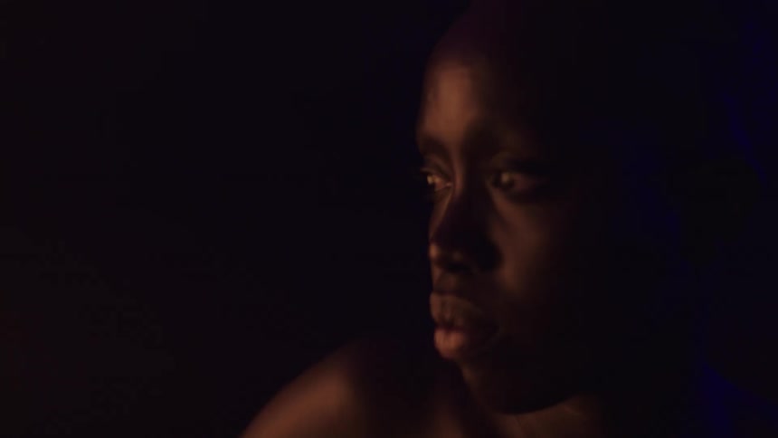 A young black woman sits in a dark room moving her neck back and forth