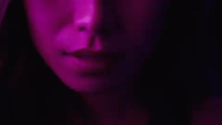 A closeup shot shows a persons mouth and chin under a purple light the person appears to be speaking