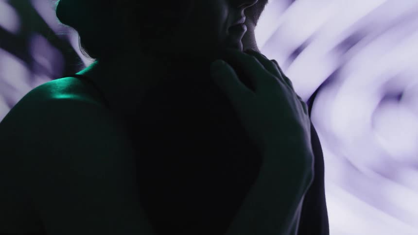 A couple hugs in front of a screen displaying a blurry image