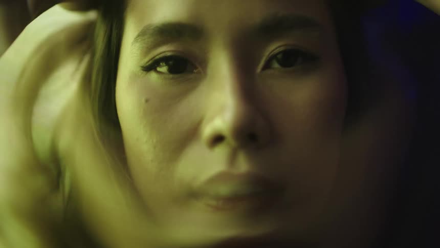 A young woman sits in a room with a large monitor behind her displaying a distorted image