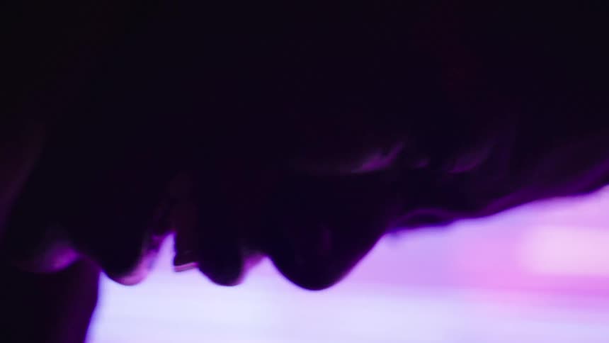 A young woman kneels in a dark room illuminated by light reflecting from a large screen crying in sadness