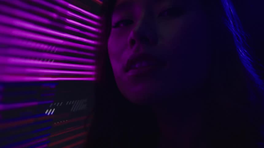 Woman closely looks at a wall lit by green and colorful lights