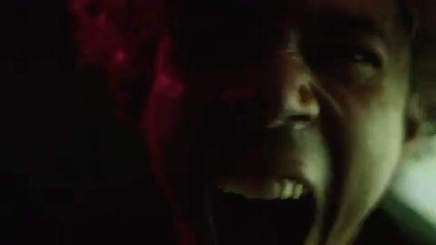 A young mans face only partially illuminated by blue and pink flashing lights as he screams in anger