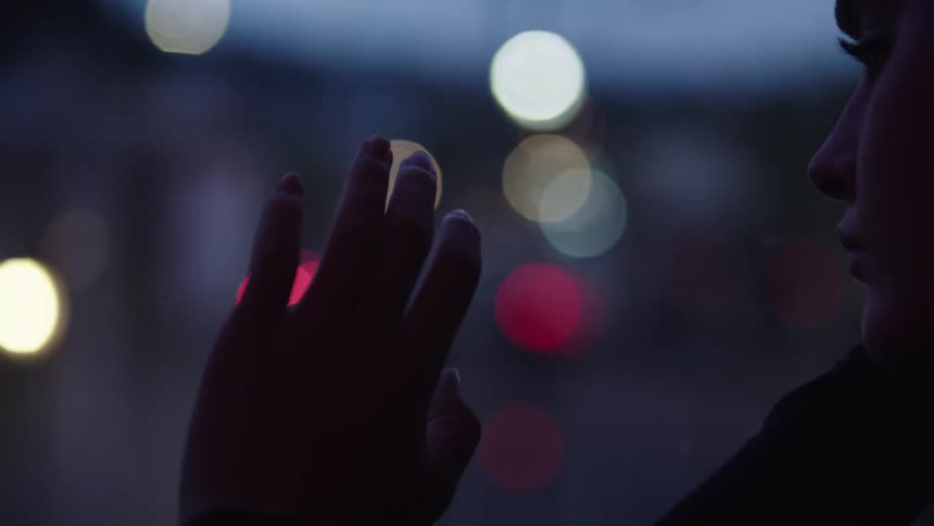 A silhouetted hand reaches toward a softly blurred cityscape with colorful bokeh lights at dusk