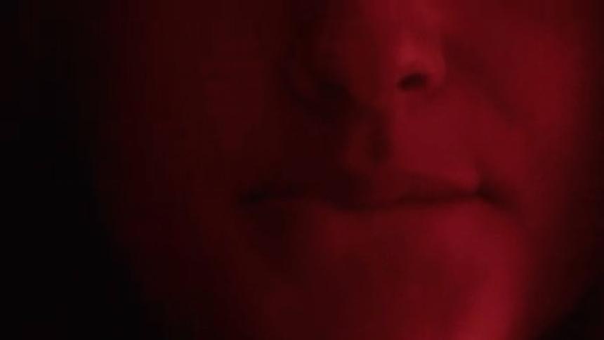 A young woman in a dark room illuminated by red light folds her lips