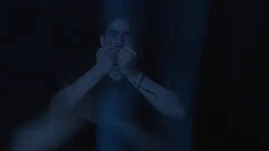 A young man sits with his hands over his face inside a dark room with flashing lights