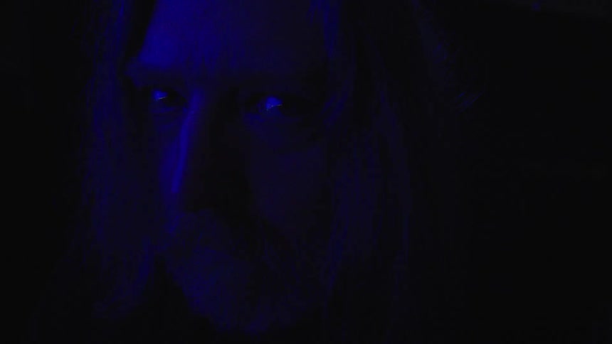 A mans serious face in the dark as blue light falls on him and he turns his eyes to the side
