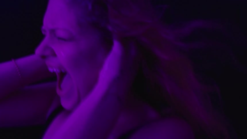 Woman screams with hands on ears under intense purple light