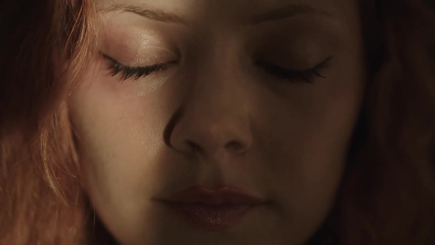 A closeup shot focuses on a womans face as she closes her eyes with a beam of light illuminating her features