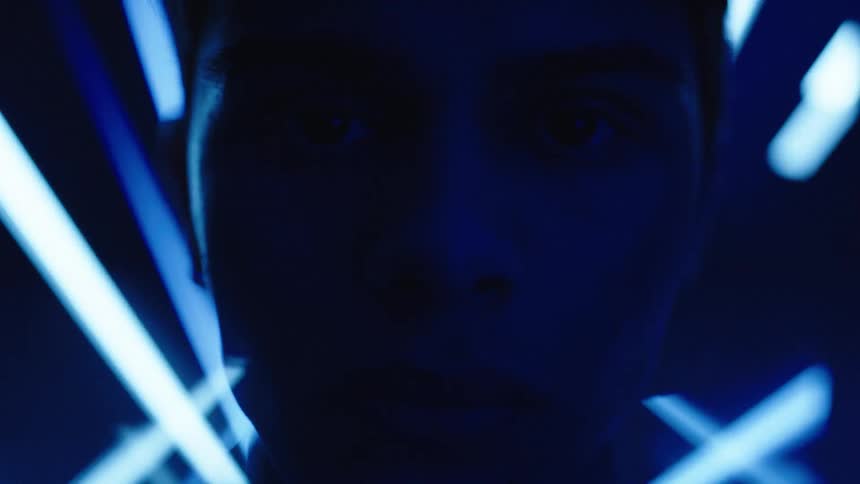 Face partially lit by blue neon lights in a dark setting