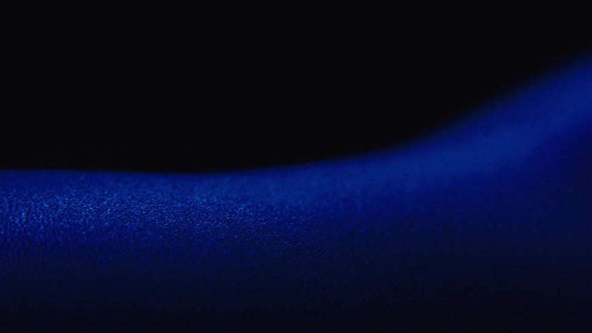 A smooth surface is illuminated by deep blue light against a black background