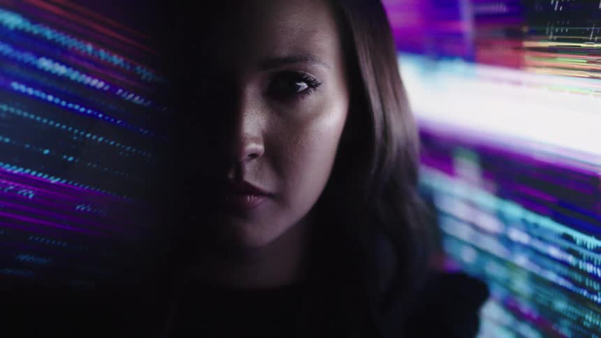 Woman stares at the camera with a background lit by purple and blue lights