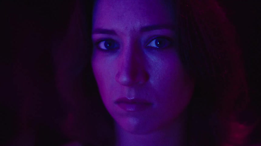 Female face lit by purple and blue lights against a dark background