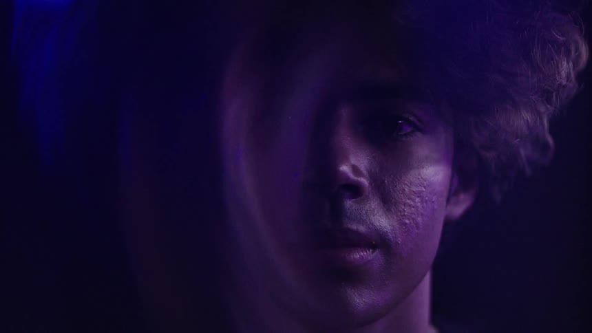 Male face in closeup with blue and purple lighting against a dark background