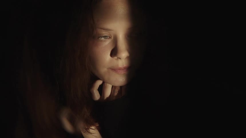 A closeup of a persons face is shown with a serious expression as light and shadow shift across the persons features