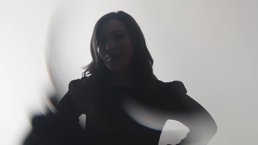 A woman is shown in a outoffocus white background raising their arm with a sense of fluid silhouetted motion