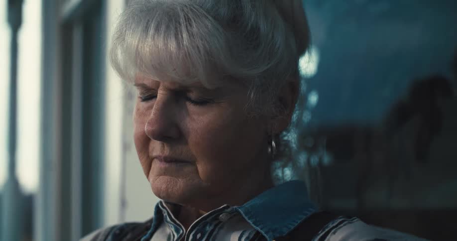 Elderly woman with closed eyes in a serene expression lit by natural light