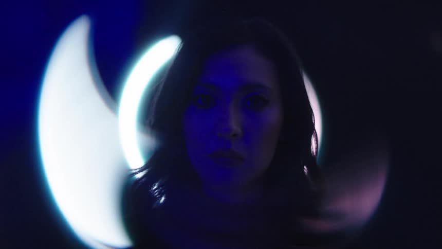 A womans face is shown in profile with a sad expression as a glowing circular light behind her casts a soft glow on her features
