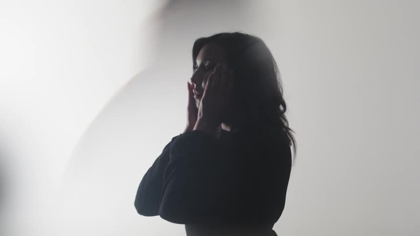 A dark silhouette of a woman is shown against a bright white background with her shadow cast on the wall behind her