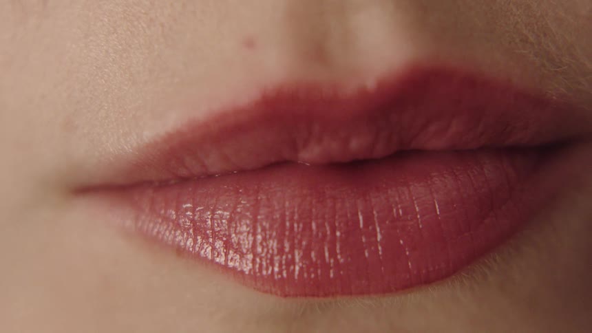 A close view shows a persons mouth with shiny pink lipstick the lips moving from a relaxed position to a wide smile that reveals a row of straight white teeth and then returning to a neutral expression
