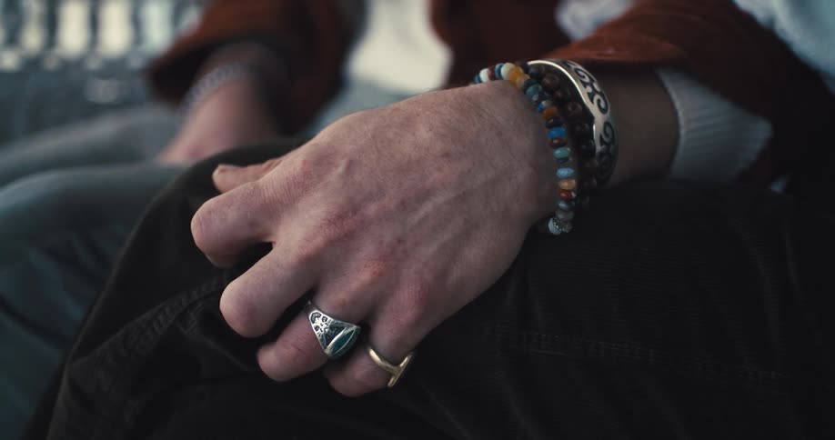 Person wearing bracelets and rings strokes the knee of another person through their clothes