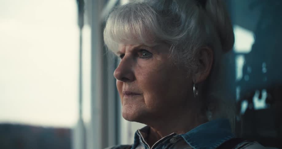 An elderly woman with her gray hair in a bun with a pensive expression