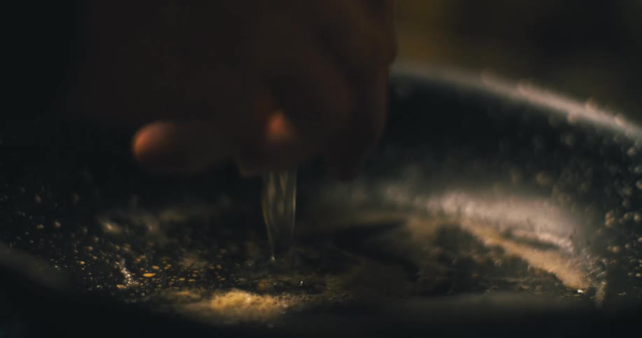 A person cracks an egg on the side of a skillet then breaks the shell and drops the egg into the skillet revealing a bright yellow yolk and the egg white