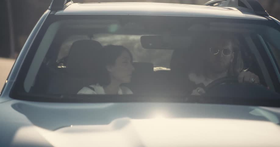 A sunny wide shot of two people inside a moving car their faces obscured by bright sunlight