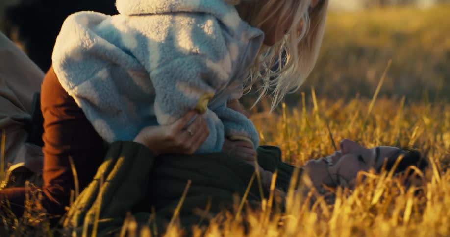A mother holds and plays with her toddler while lying on a grassy field at midday both having fun