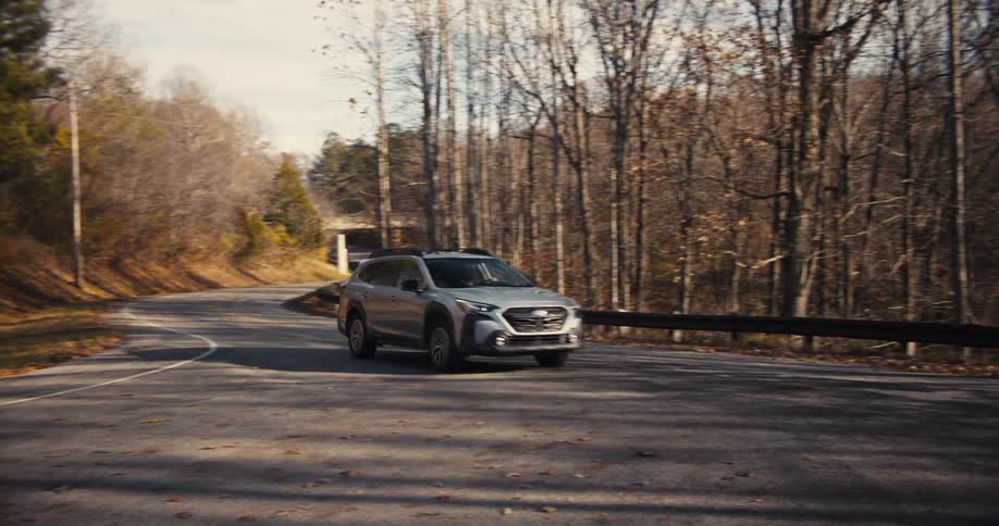 A gray suv is driving on a winding twolane road in a scenic wooded area