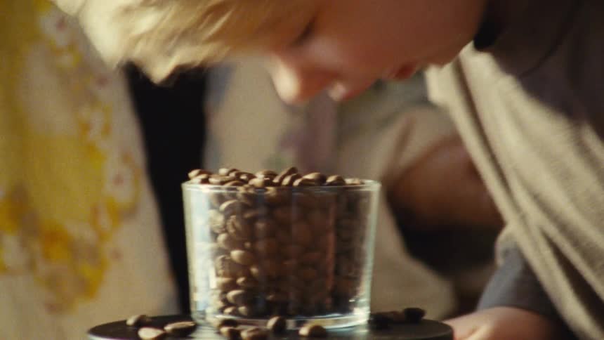 A boy pressing his face into a cup full of coffee beans