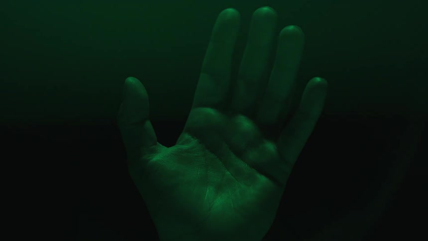A person holds their open hand up as a dim light overhead changes color