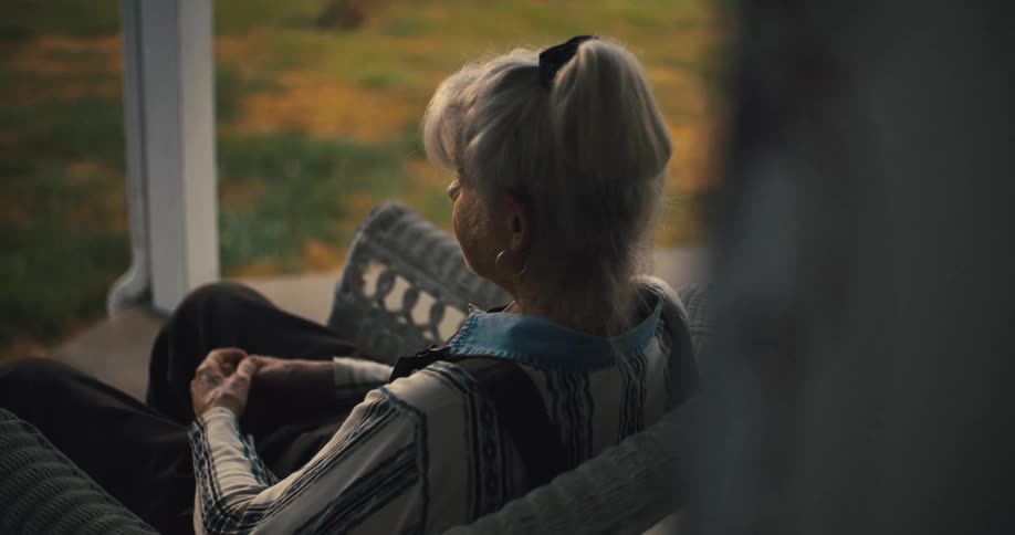 Elderly woman sitting on a wicker chair observing the backyard