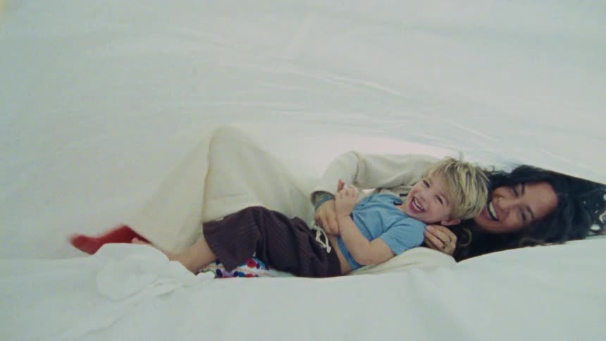 Mother and son joyfully cuddle and laugh under white sheets