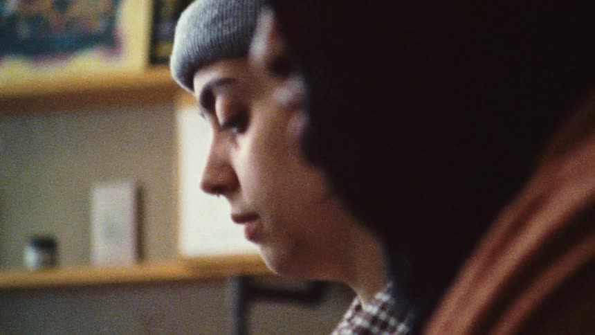 A young woman wearing a beanie hat and earrings is busy in a kitchen with a young man