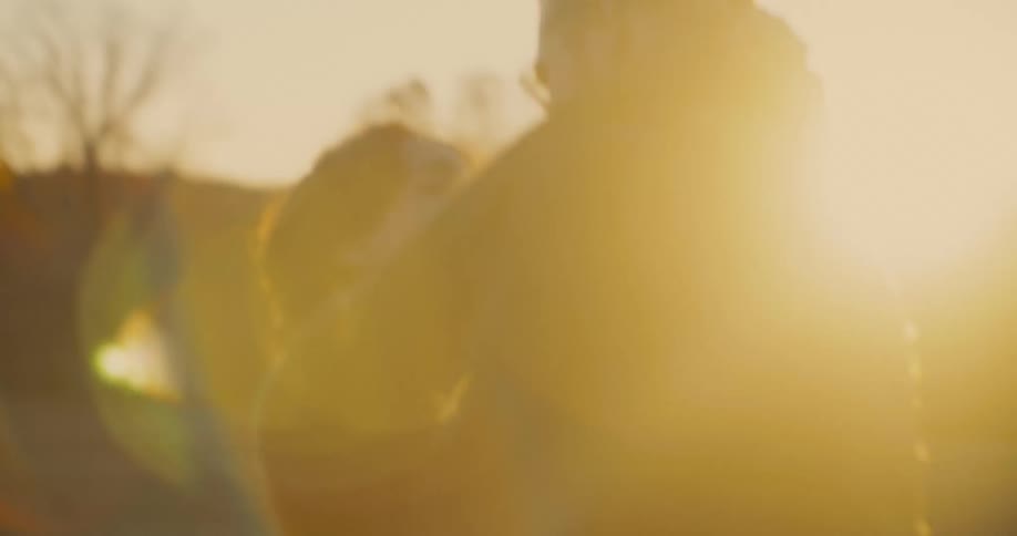 A blurry view of a man and a woman embracing outdoors in a field with the setting sun creating a bright golden lens flare and silhouetting them