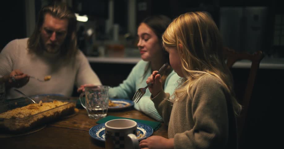 Three people a father and his two daughters sit at the dining table having dinner