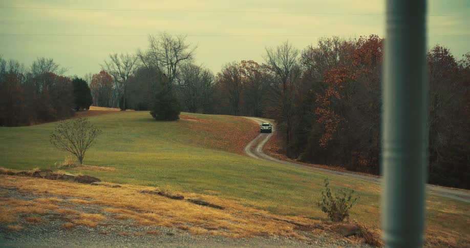 Car drives on a winding rural road through fields and trees