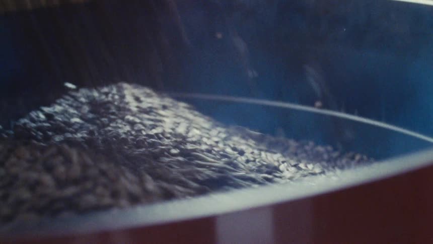 A view of a coffee bean roaster shows a large drum filled with dark brown roasted coffee beans