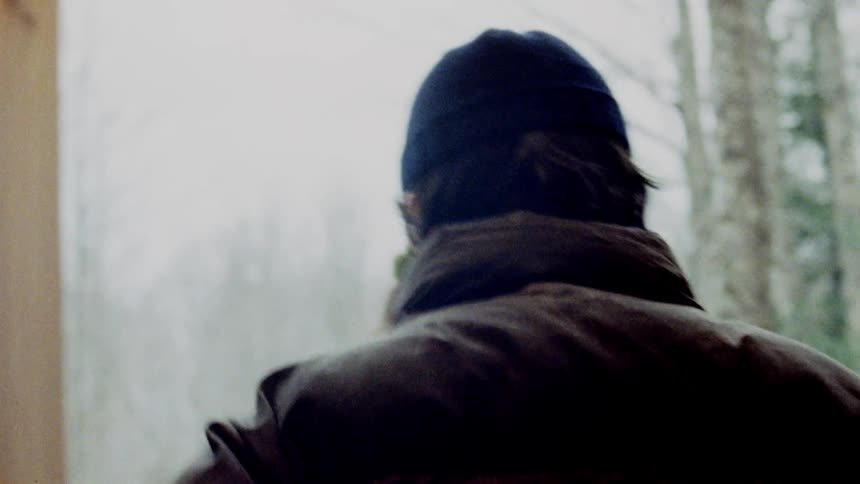 Two people walking out of a wooden cabin into the winter landscape