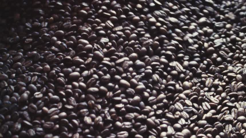 A very close view shows dark roasted coffee beans tumbling in a roaster drum