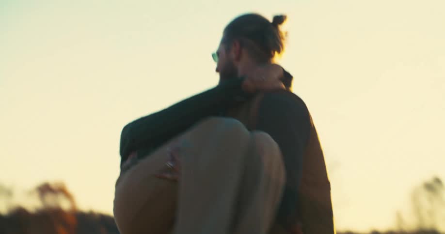 Man carries woman in his arms outdoors during sunset