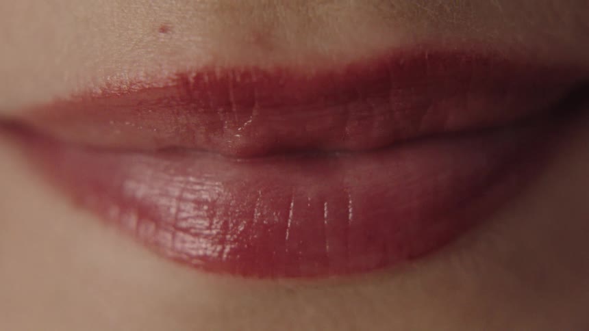 The video shows an extreme closeup of a persons mouth with their lips parted in a slight smile revealing their teeth the lips appear glossy with a hint of red color