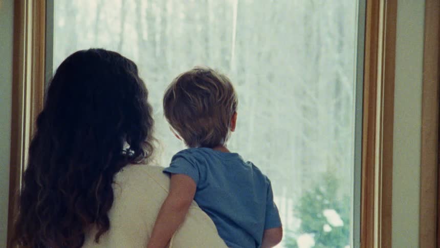 A woman holds a boy while they look out at snow