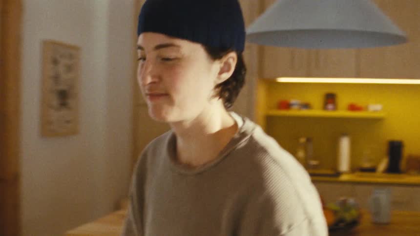 A teenage boy wearing a black cap and a brown tshirt walks through a kitchen at midday