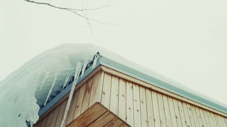 A wooden cabin roof covered in snow with long icicles hanging down