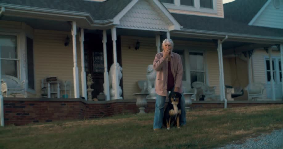 Elderly woman waves in front of the house with a dog