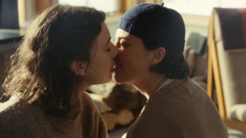 Two women share a kiss in a warmly indoors